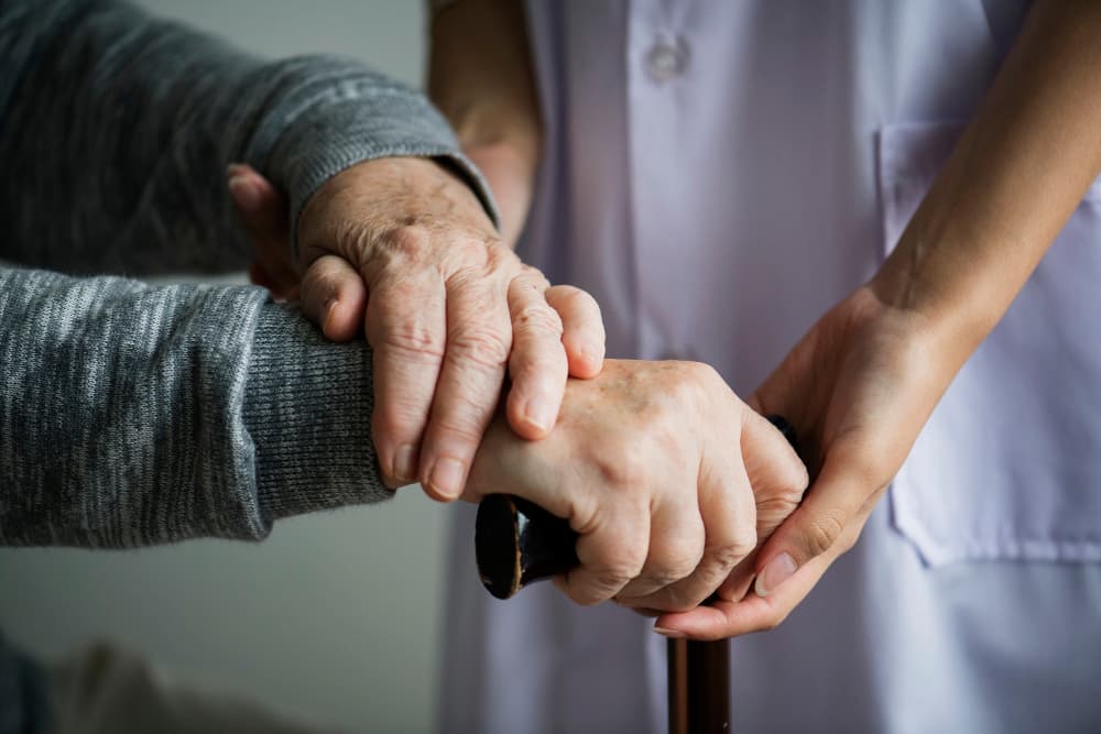 manos de un cuidador sosteniendo las manos de un adulto mayor
